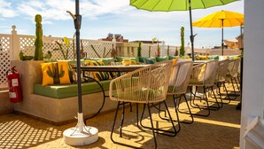 An outdoor seating area with cushioned sofas and metal chairs, surrounded by cacti and a white lattice fence. - Riad Jaia (Marrakech)