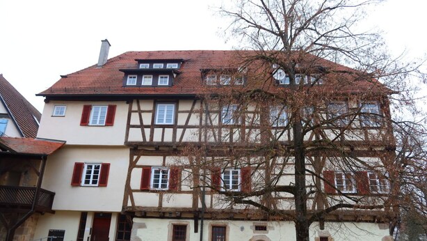 Une maison traditionnelle à colombages, dotée d’un toit à forte pente, de nombreuses fenêtres avec volets et d’un petit escalier menant à l’entrée.