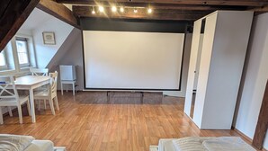 Une chambre confortable située dans les combles, avec un plancher en bois, un plafond blanc et un écran de projection.
