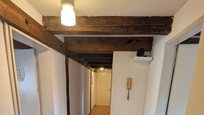 Un couloir doté d’un plancher en bois, de murs blancs et de poutres apparentes. Des portes se trouvent de part et d’autre, dont une sur laquelle est fixé un téléphone au mur.