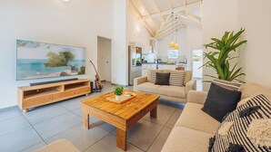 Ein geräumiges Wohnzimmer mit einem großen Flachbildfernseher, einem Holztisch und einer Couch mit gestreiften Kissen.