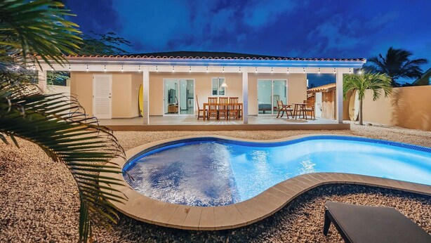 Ein modernes Haus mit Swimmingpool, einer überdachten Terrasse und Blick auf den Nachthimmel.