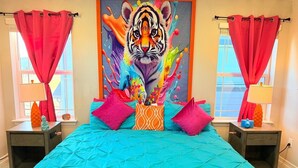 Une chambre à coucher avec une couvre-lit turquoise, un tableau représentant un tigre aux couleurs vives et des rideaux roses.