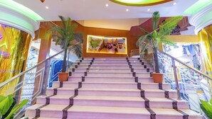 A grand staircase with marble steps and metal railings, leading to a reception area with a world map and a photo of three individuals. - Sama Almisk Hotel (Makkah)