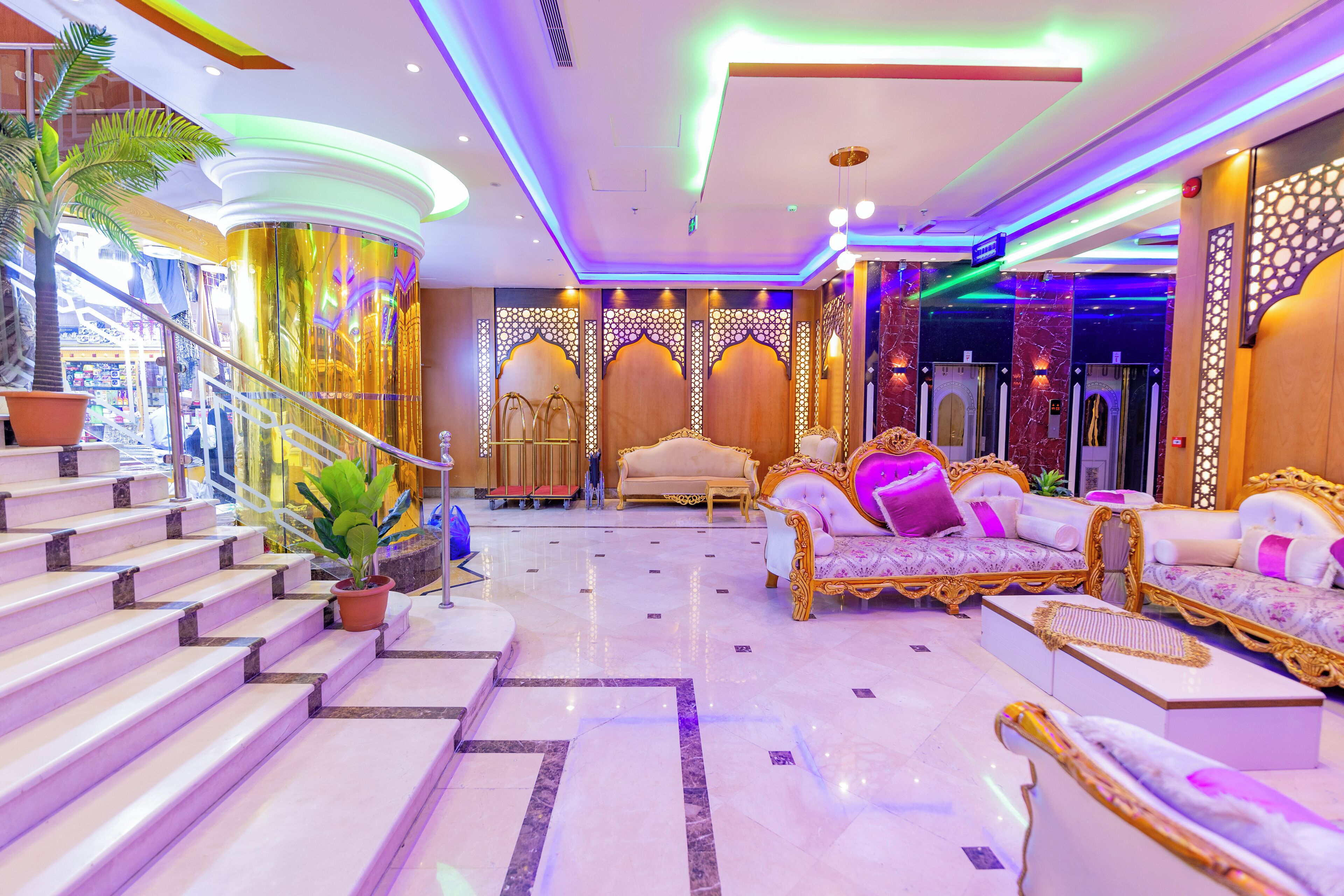 A luxurious lobby with marble flooring, ornate sofas, and a staircase with a potted plant.