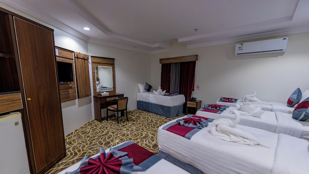 A hotel room with four beds, a desk, a chair, and an air conditioning unit. - Sama Almisk Hotel (Makkah)