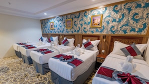 A hotel room with four beds arranged in a row, each with neatly made beds and towels. - Sama Almisk Hotel (Makkah)