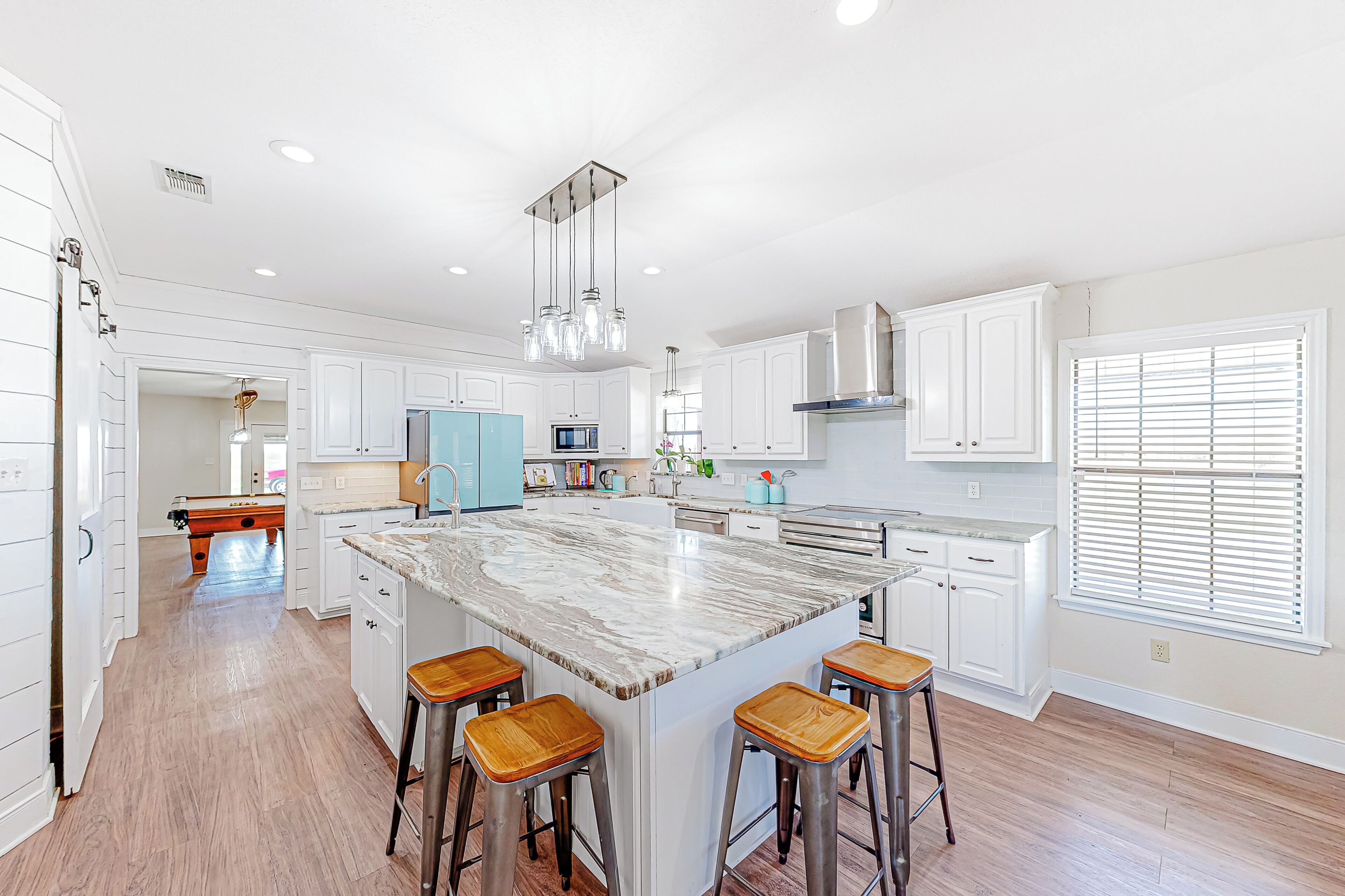 A spacious kitchen with white cabinetry, a large island with stools, and a view of the adjacent living area.