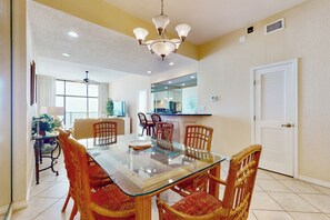 A dining area with a glass-top table, wooden chairs, and a chandelier. - 2BR PH, Epic Gulf Views: Suntide III - Unit 1104 (South Padre Island)