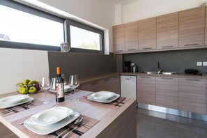 A modern kitchen with wooden cabinets, a built-in dishwasher, and a dining area set with plates, glasses, and a bottle of wine. - Villa Alen – Exclusive Luxury Escape with Private Pool & Breathtaking Views (Chania)