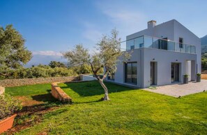 Ein modernes, zweistöckiges Haus mit einem Glasbalkon, umgeben von einem gepflegten Rasen und Bäumen.