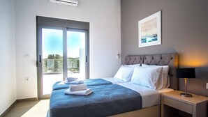 Una habitación de hotel moderna con una cama grande, una mesita de noche con lámpara y vistas al exterior a través de una puerta corredera.