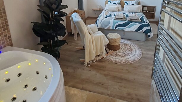 Une chambre moderne avec un grand lit, une chaise, une petite table ronde et une baignoire équipée de lumières.