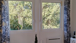 Un coin repas avec une table ronde en verre, deux chaises et une vue sur les arbres à travers deux fenêtres.