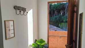 Une pièce avec un banc blanc, un luminaire fixé au mur, un certificat encadré et une porte donnant sur un espace extérieur doté d’un sol carrelé et d’un paillasson.