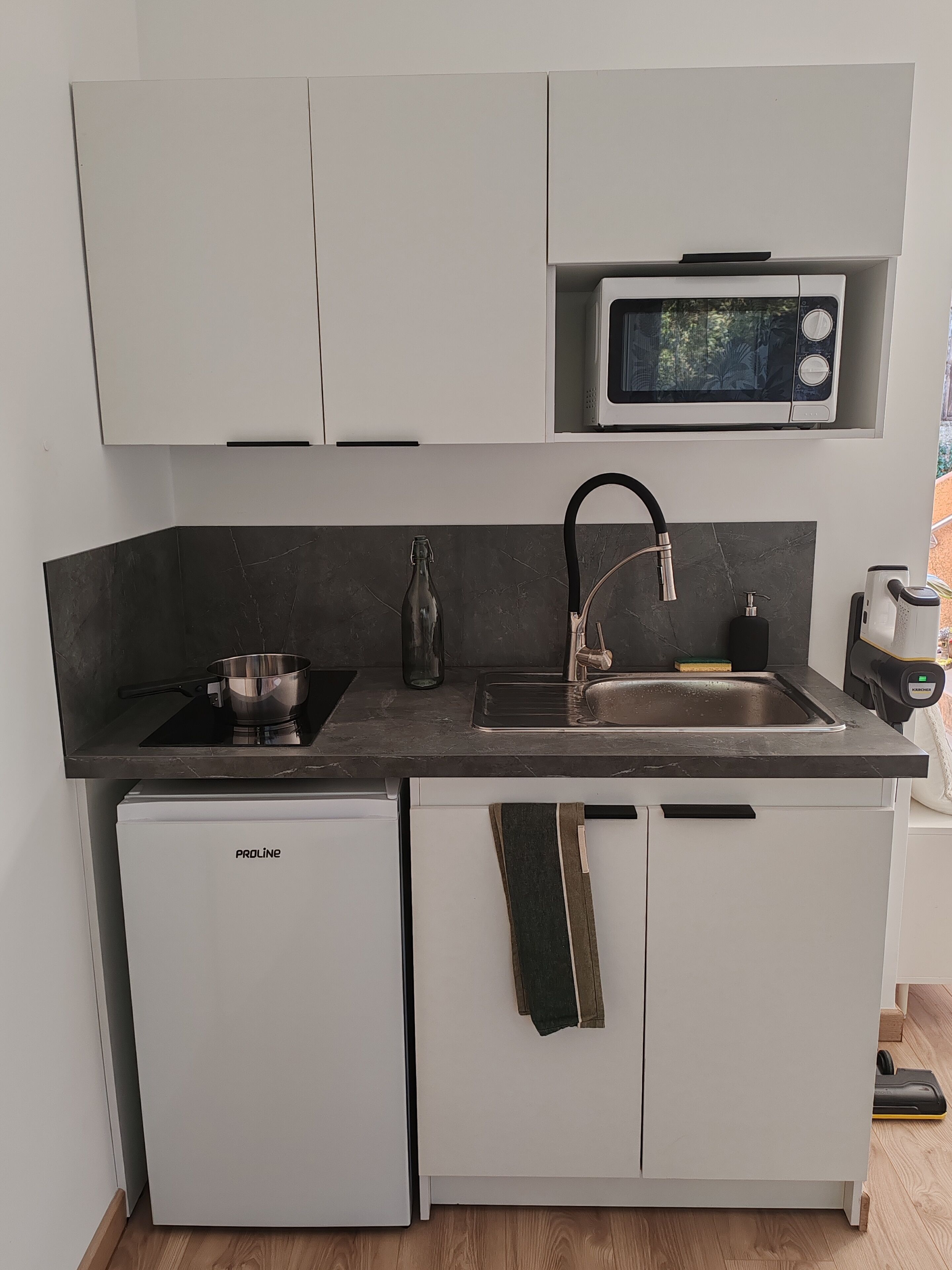 Ett kompakt kök med mikrovågsugn, diskho, spis och ett litet kylskåp.