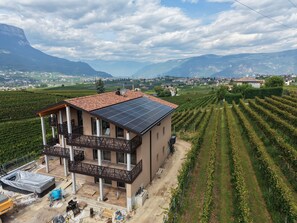 Ein zweistöckiges Gebäude mit Balkon, Solaranlage und einem Weinberg im Hintergrund.
