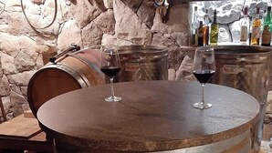 A large wooden barrel table with two wine glasses on top, set against a stone wall with bottles in the background. - New vacation apartments in the middle of the vineyards (Eppan an der Weinstraße)