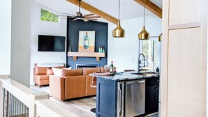 A modern living room with a sofa, a fireplace, and a kitchen island with a sink and dishwasher. - NEW - Luxury Mountain Retreat - Walk to Redtail Vineyard (Blairsville)