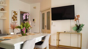 Ein Essbereich mit einem weißen Tisch, Stühlen und einem an der Wand montierten Fernseher.