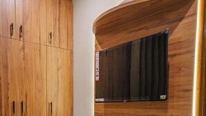 A room with a wooden wardrobe, a small table, a shelf with a kettle, and a patterned rug. - MG Luxury Stays (Panchkula)