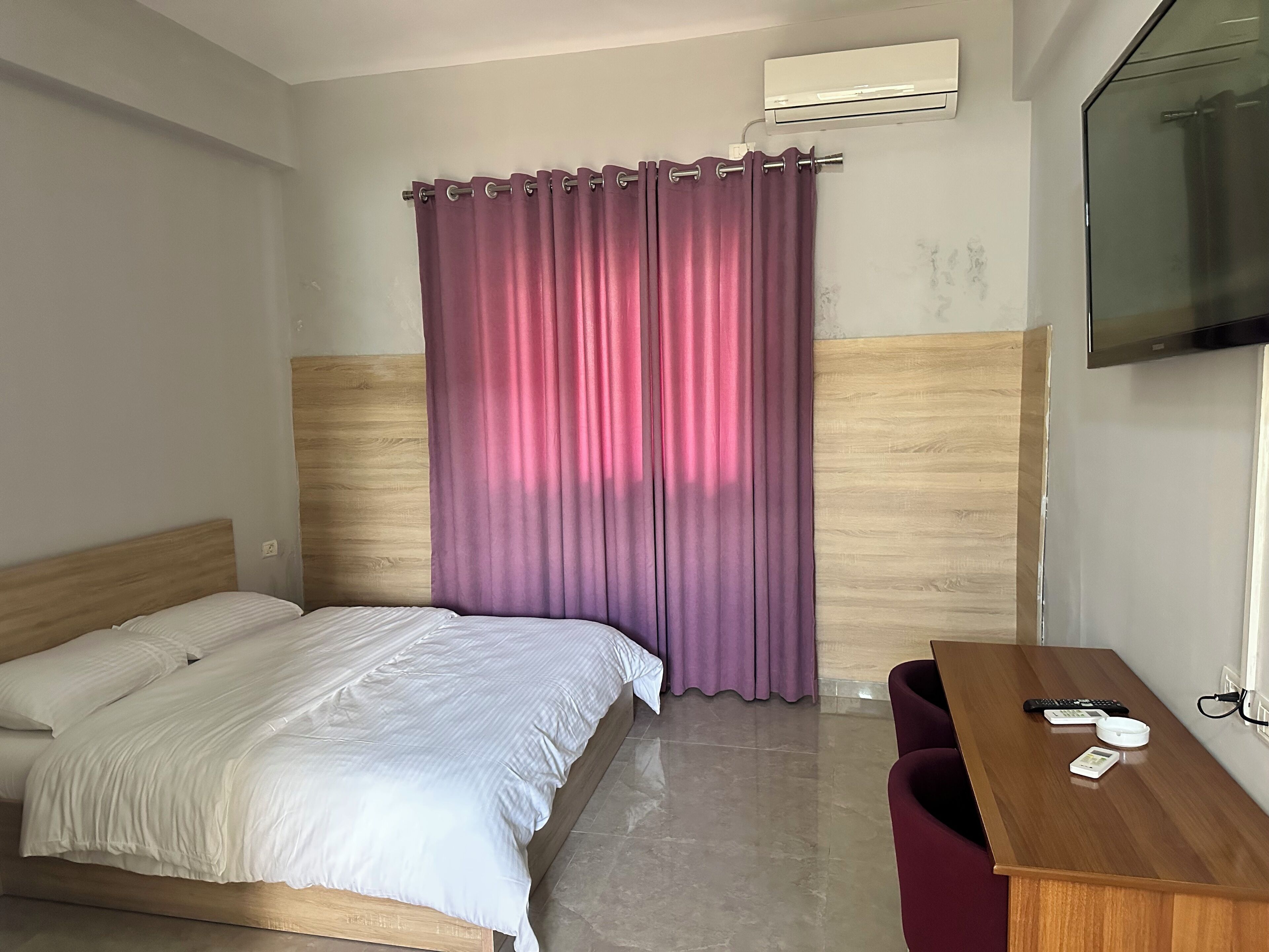 Ein Hotelzimmer mit einem Bett, einem Schreibtisch, einem Stuhl, einer Klimaanlage und einem Fernseher.