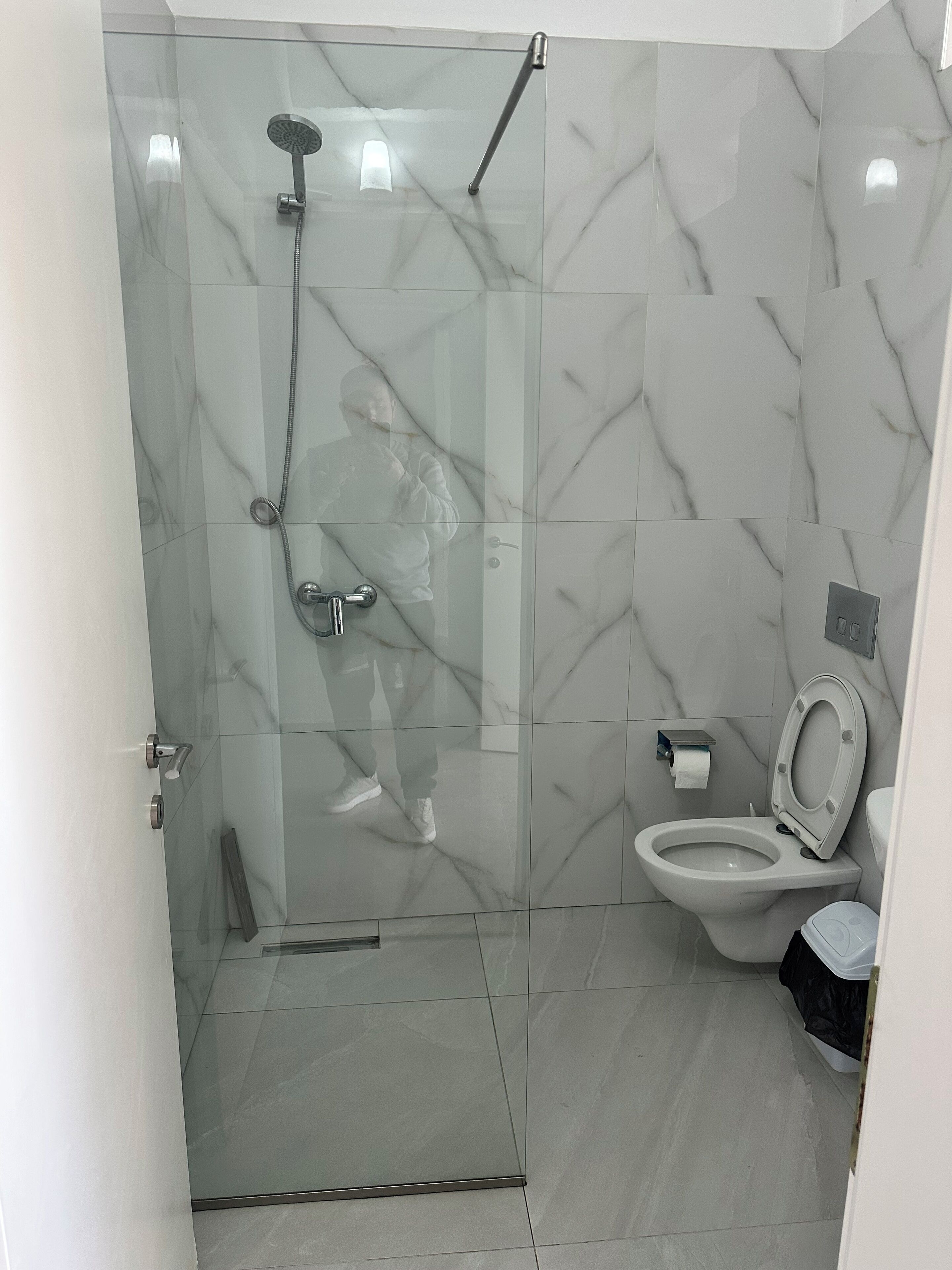 Un baño con ducha de vidrio, inodoro y suelo de mármol.
