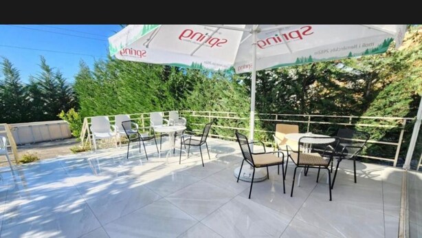 Ένας εξωτερικός χώρος με τραπέζι και καρέκλες, σκεπασμένος με μια ομπρέλα που φέρει το λογότυπο της εταιρείας.