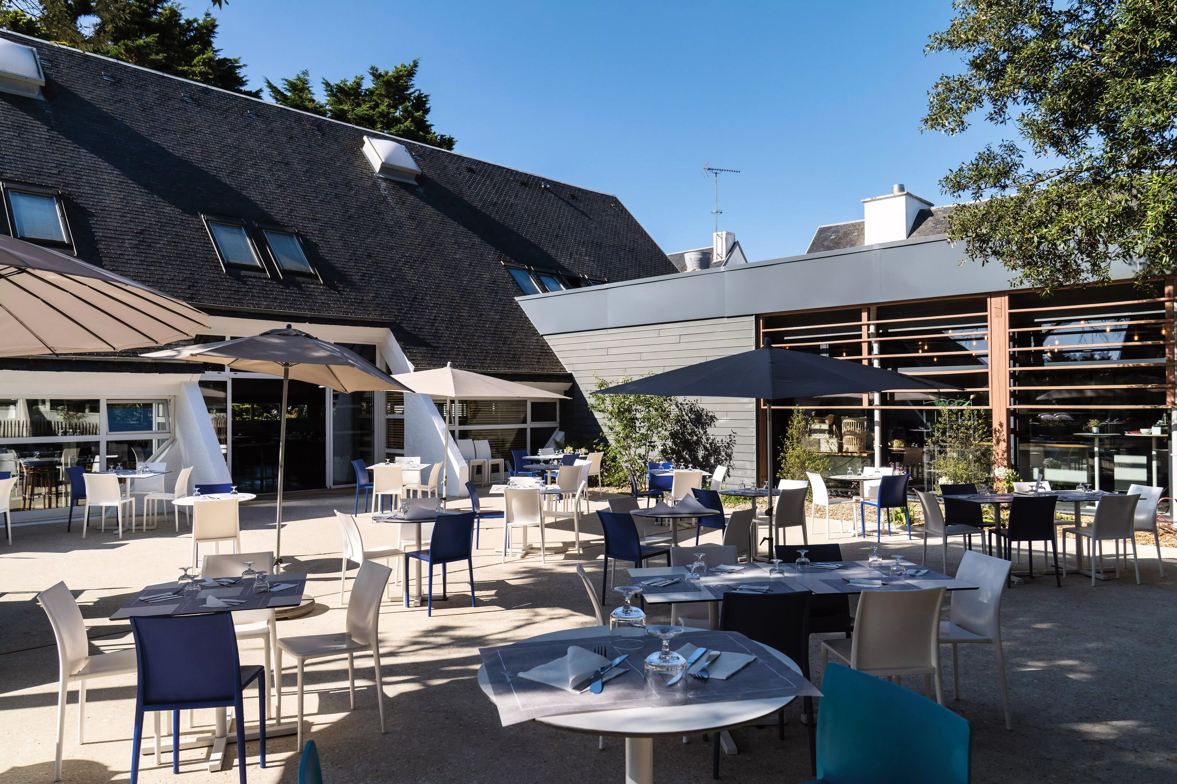 Un espace extérieur aménagé avec des tables et des chaises, un bâtiment doté d’un toit en pente et un ciel dégagé.