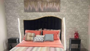 A bedroom with a brick-patterned wall, a bed with a black upholstered headboard, and two bedside tables. - Spacious 3BR Home w/ Office & Backyard Vibes – Near Frisco. (Aubrey)