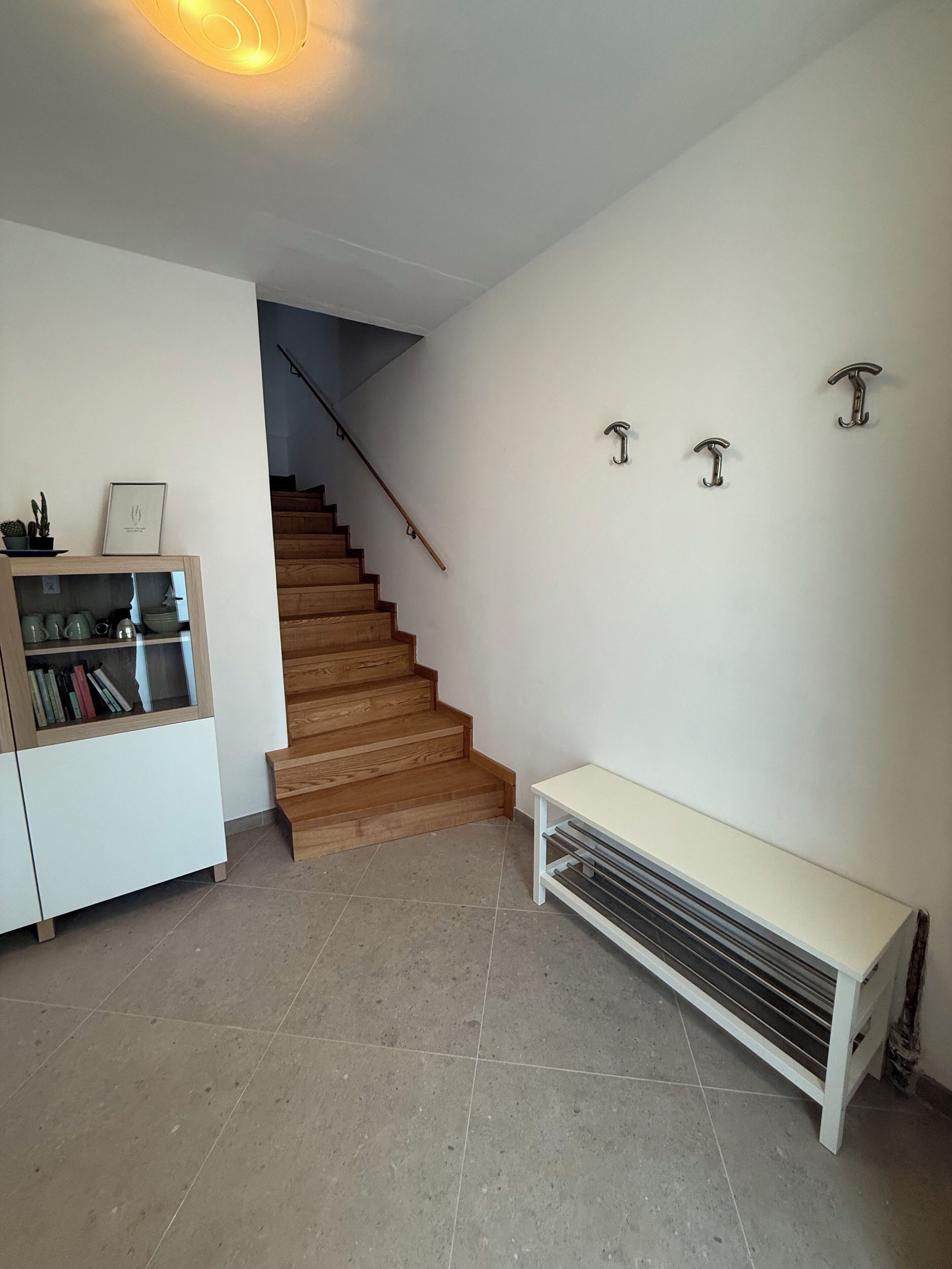 Un escalier menant à un palier où se trouvent un banc blanc et un meuble contenant des livres et des objets décoratifs.
