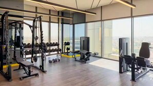 A modern gym with a variety of equipment, large windows, and a city view. - Vogue | Aykon City Business Bay near Metro Station (Dubai)