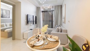 A modern living room with a dining area, a TV mounted on the wall, and a sofa. - Vogue | Aykon City Business Bay near Metro Station (Dubai)