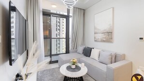 A modern living room with a grey sofa, a round coffee table, and a large window with curtains. - Vogue | Aykon City Business Bay near Metro Station (Dubai)