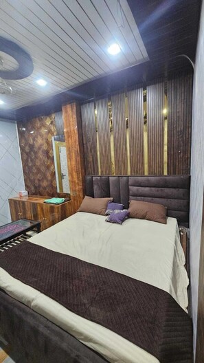 A modern bedroom with a large bed, a wooden headboard, a nightstand, and a dresser. - Heritage Heaven Home Stay (Varanasi)