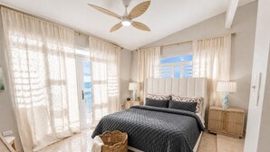 A bedroom with a bed, a nightstand, a lamp, a ceiling fan, and a view of the outside. - Extra Large Two Story Oceanfront Home | 10 mins from Rincón & Aguadilla | ON THE BEACH SLEEPS 24 PLUS (Bo Espinar Aguada)