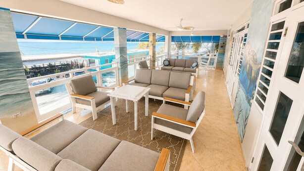 A spacious balcony with a view of the sea, furnished with sofas and a table. - Extra Large Two Story Oceanfront Home | 10 mins from Rincón & Aguadilla | ON THE BEACH SLEEPS 24 PLUS (Bo Espinar Aguada)