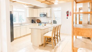 A modern kitchen with wooden ceiling beams, a central island with chairs, and a view of the outside through large windows. - Extra Large Two Story Oceanfront Home | 10 mins from Rincón & Aguadilla | ON THE BEACH SLEEPS 24 PLUS (Bo Espinar Aguada)