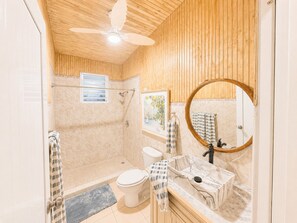 A bathroom with a shower, toilet, sink, and a ceiling fan.