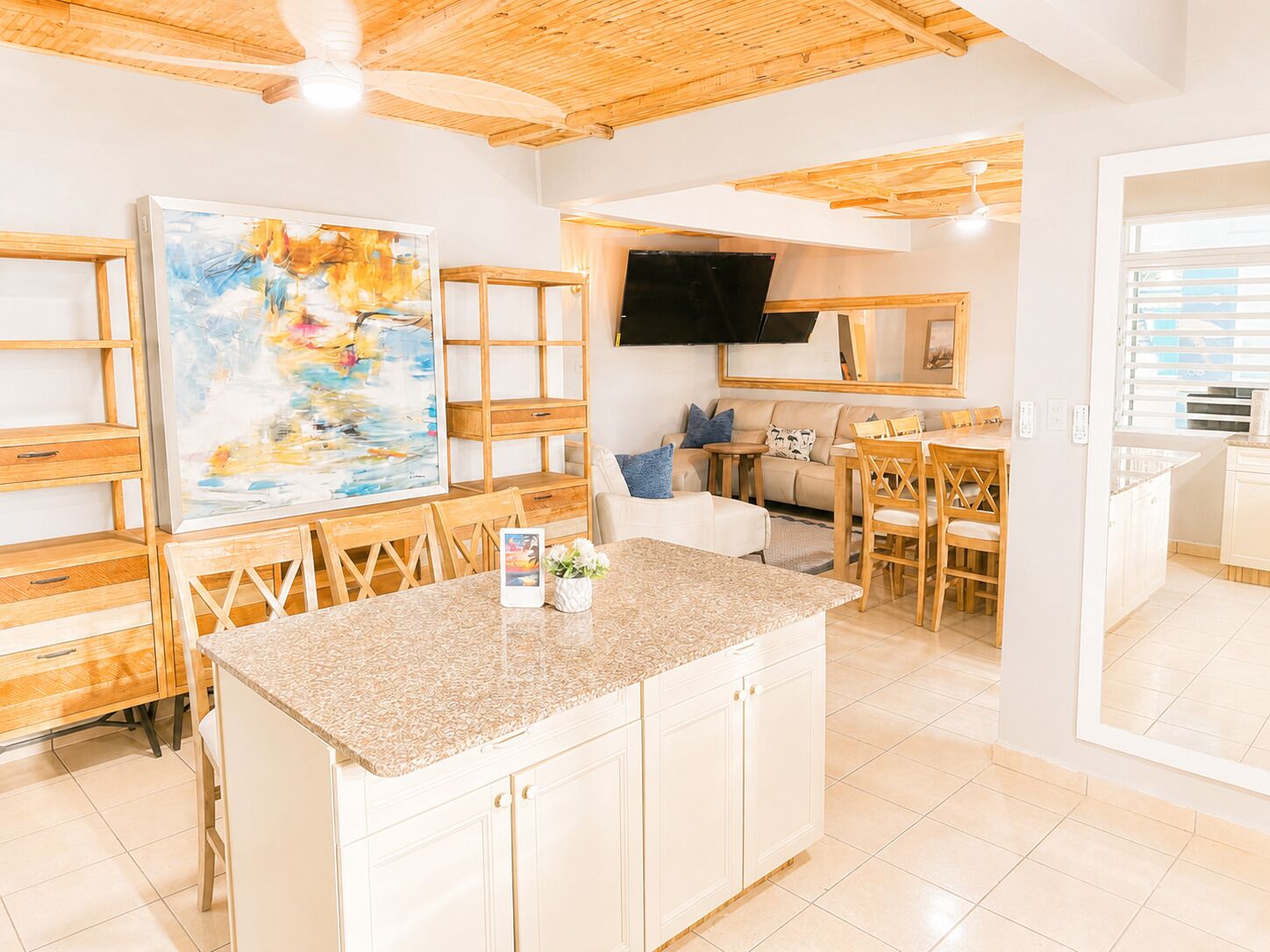 Eine moderne Küche mit einer Granitabdeckung, Holzschränken, einem Essbereich mit Tisch und Stühlen, einer Couch und einem großen, abstrakten Gemälde an der Wand.