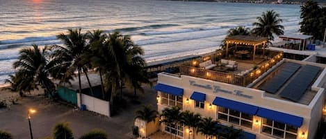 A beachfront hotel with a patio area, palm trees, and a sunset view.
