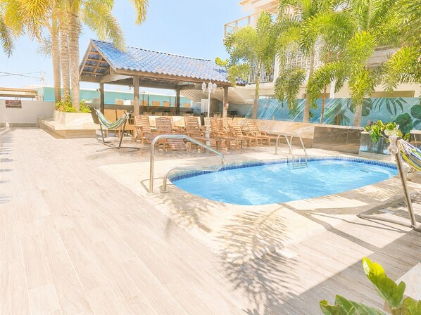 A swimming pool with lounge chairs and a covered seating area.