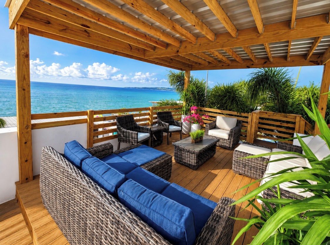 Un espace extérieur abrité avec des meubles en osier, une terrasse en bois et une vue sur l’océan.