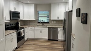 A modern kitchen with white cabinets, stainless steel appliances, and a window with blinds. - 3 bed/2 bath pool home & hot tub in Naples. Great neighborhood. 3 miles to beach (Naples)