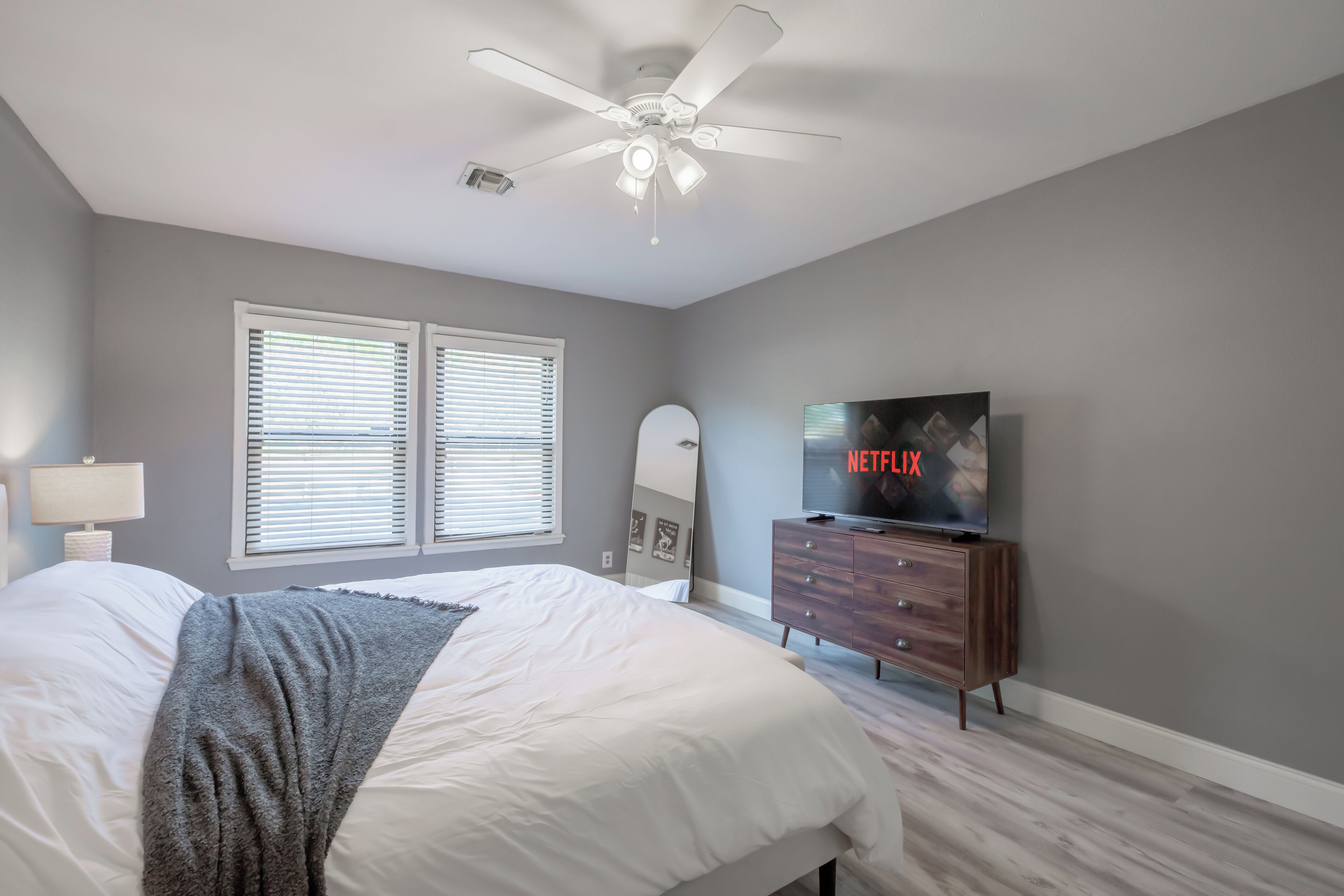 Une chambre à coucher avec un lit, un ventilateur de plafond, une télévision et une commode.