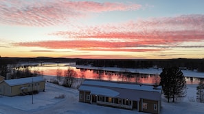 A winter landscape with a river, a bridge, and buildings with snow-covered roofs.