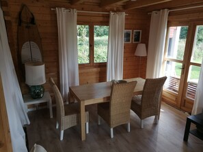 A wooden cabin with a dining table, wicker chairs, a lamp, and a view of greenery outside. - Cozy "Heimathafen" vacation home in Wiek on Rügen, right on the waterfront (Wiek)