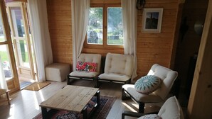 A cozy room with wooden walls, a sofa, two armchairs, a coffee table, and a rug.