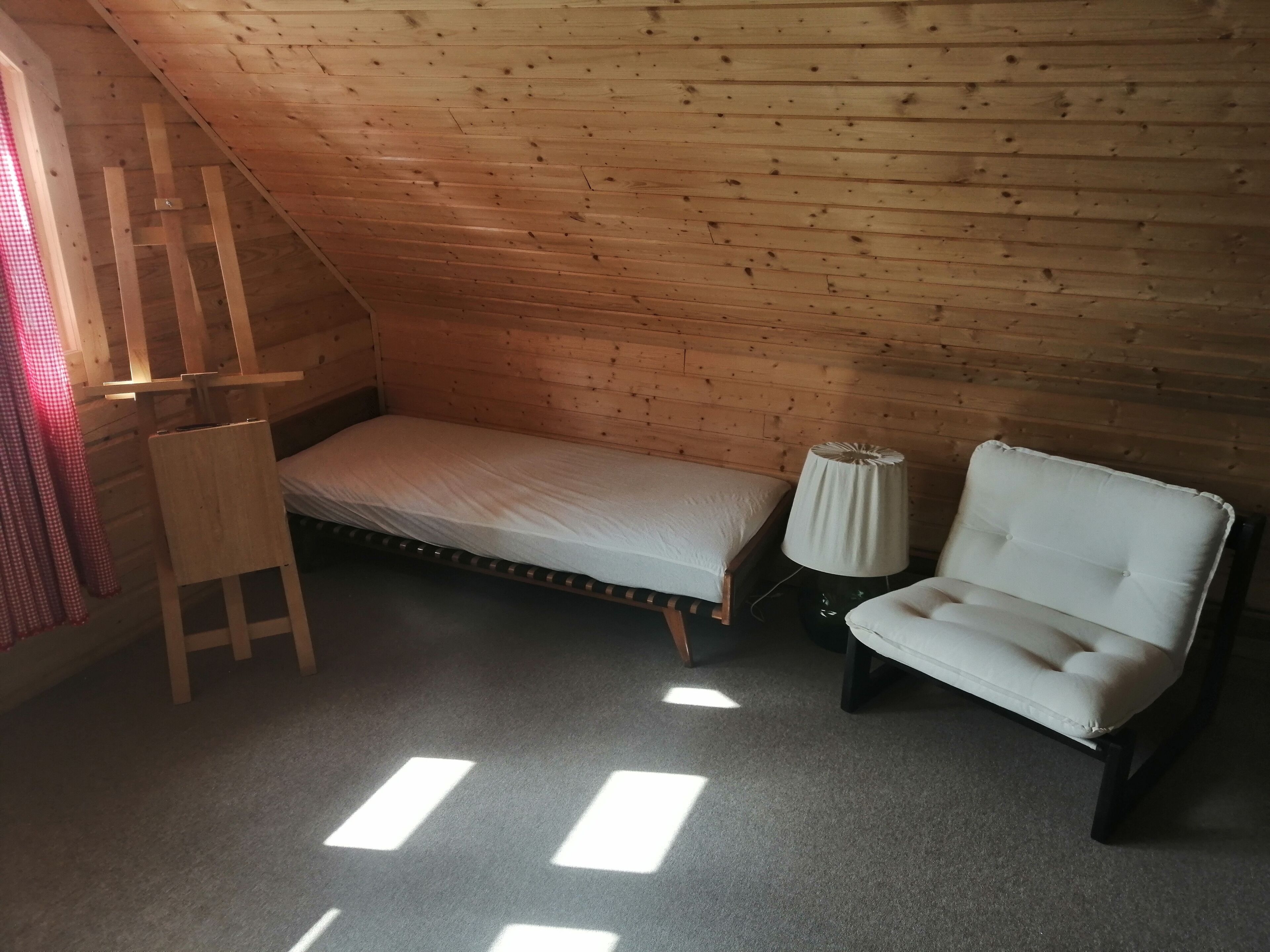 Habitació petita i acollidora amb sostre inclinat, un llit individual, una cadira i una taula petita.