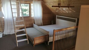 A wooden cabin room with a loft bed, a ladder, a small table, and a hanging light fixture.
